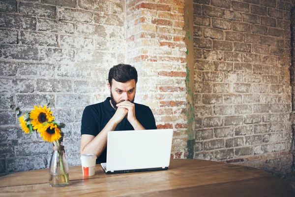 Homem barba jovem concentrado trabalhando no laptop enquanto sentado no local de trabalho — Fotografia de Stock