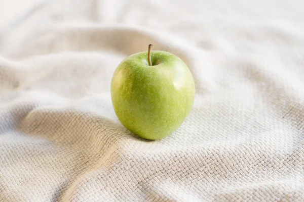 Close-up of single green juicy apple on the table with white tablecloth. Food photography using natural window light. Eating green apples helps increasing the body\'s metabolism.