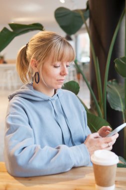 Modern kafede kahve içerken cep telefonuyla el ele tutuşan bir kadının fotoğrafı. Birlikte çalışıyoruz. Haberler, sosyal ağlar, internette akıllı telefondan sörf yapmak. Kahve molası işi..