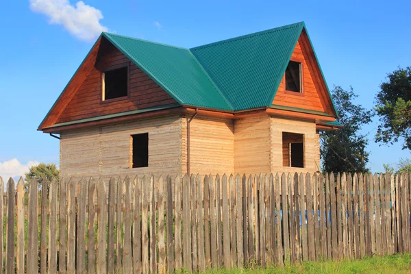 Wooden house under construction behind the fence — Stock Photo, Image