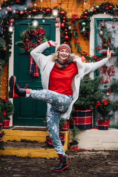 woman  in red funny  sing song dancing in decorated illuminated twinkle lights glowing xmas tree near house