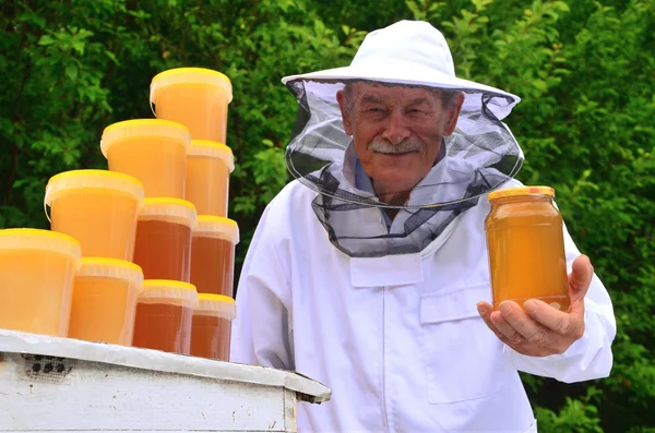 Coleccionista senior presentando tarro de miel fresca en colmenar en primavera —  Fotos de Stock