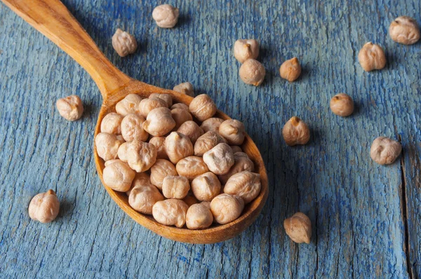 Garbanzos crudos en una cuchara de madera de cerca en una mesa vieja — Foto de Stock