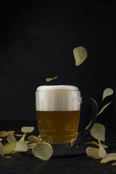 Cerveja com batatas fritas voadoras em um fundo preto — Fotografia de Stock