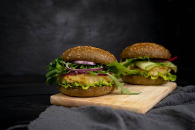 Vejetaryen Amerikan mutfağı. Balıklı hamburger, roka, salatalık. Siyah arka planda bir burger..