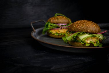 Vejetaryen Amerikan mutfağı. Balıklı hamburger, roka, salatalık. Siyah arka planda bir burger..