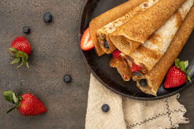 Tahta masadaki tavada böğürtlenli ev yapımı kırsal krep. Masa üstü görünümü. Maslenitsa yemeği.