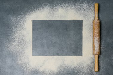 Koyu bir yüzeyde yuvarlak iğne ve beyaz un. Yazı için boş yer var. Üst görünüm.