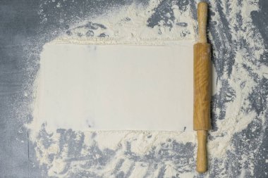 Koyu bir yüzeyde yuvarlak iğne ve beyaz un. Yazı için boş yer var. Üst görünüm.