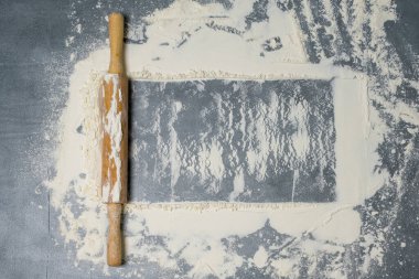 Koyu bir yüzeyde yuvarlak iğne ve beyaz un. Yazı için boş yer var. Üst görünüm.