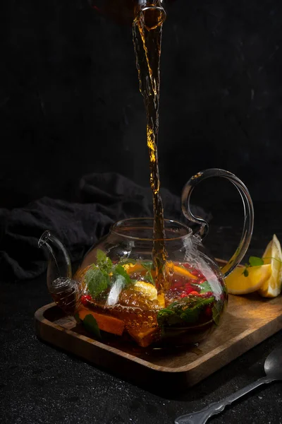 Pour black tea from a transparent teapot into a cup on black backround — Stock Photo, Image