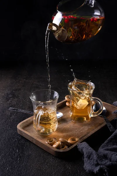 Pour black tea from a transparent teapot into a cup on black backround — Stock Photo, Image