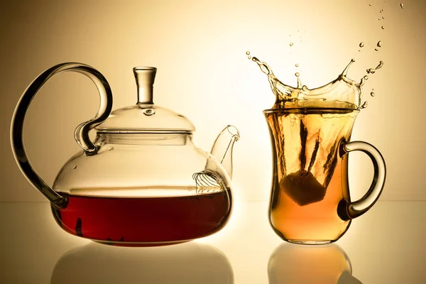 Cup of tea and glass teapot on glass with orange background — Stock Photo, Image
