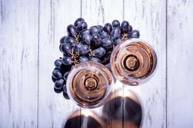 İki bardak gül şarabı ve açık ahşap masada üzümler.