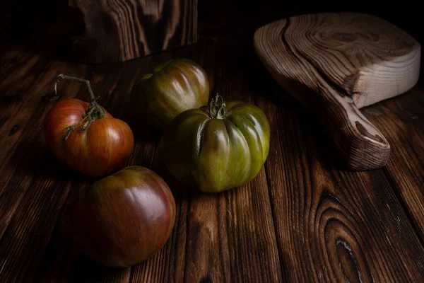 Tomates com nervuras vermelhas em uma bela tábua de corte de madeira em um fundo de madeira. Foto chave baixa. — Fotografia de Stock