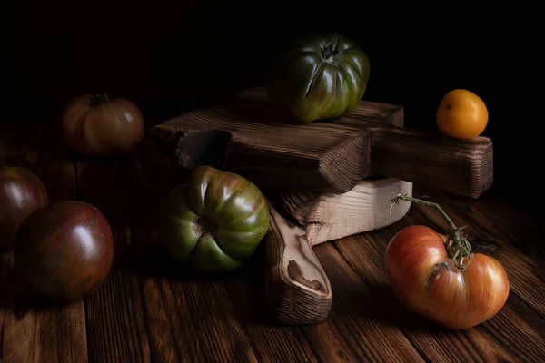 Tomates com nervuras vermelhas em uma bela tábua de corte de madeira em um fundo de madeira. Foto chave baixa. — Fotografia de Stock