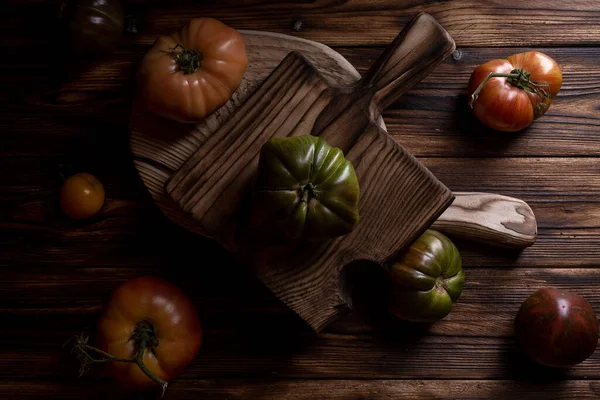 Tomates com nervuras vermelhas em uma bela tábua de corte de madeira em um fundo de madeira. Foto chave baixa. — Fotografia de Stock