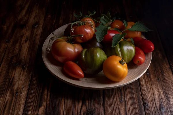 Tomates frescos em uma chapa de madeira em um fundo de madeira escuro. A colher tomates. tecla baixa. — Fotografia de Stock