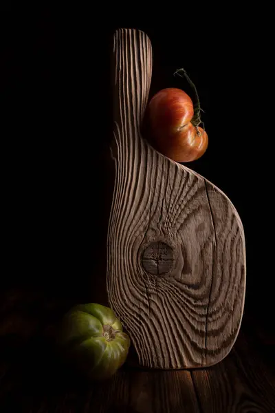 Tumpukan tomat sayuran matang segar dan papan kayu di atas meja kayu tua. Suasana pedesaan gelap. tombol rendah. — Stok Foto