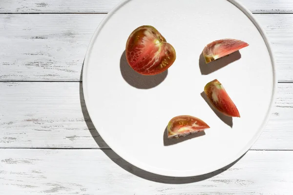 白い木の背景に影のある白い皿の上のトマト — ストック写真