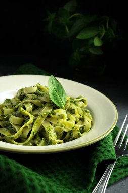 Beyaz tabakta Pesto ve siyah arka planda çatallı makarna.