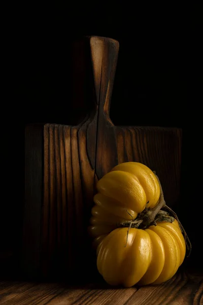 Σωρός από φρέσκες ώριμες πολύχρωμες ντομάτες λαχανικών και ξύλινη σανίδα πάνω από παλιό ξύλινο τραπέζι. Σκούρα ρουστίκ ατμόσφαιρα. χαμηλό κλειδί. — Φωτογραφία Αρχείου