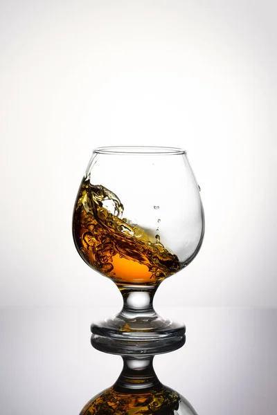 Splash cognac in glas geïsoleerd op een lichte achtergrond — Stockfoto