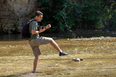 Güneşli bir günde, bir dağ nehrinde, suda dans eden genç bir adam..