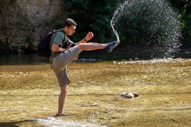 Güneşli bir günde, bir dağ nehrinde, suda dans eden genç bir adam..