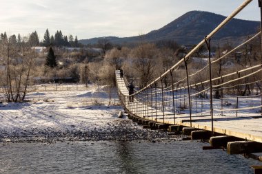 Kış günü, dağ nehri, donmayan bir dağ nehrinin üzerindeki çelik kabloların üzerinde asılı köprü, diğer tarafa gitmek için bir yol..