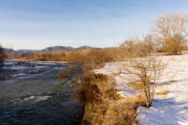 Dağ eteklerinde kış, buzsuz bir nehir, dondurucu bir sabah, yükselen güneşin ışınlarında..