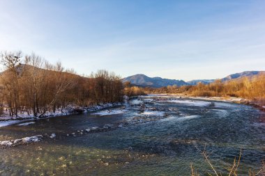 Dağ eteklerinde kış, buzsuz bir nehir, dondurucu bir sabah, yükselen güneşin ışınlarında..