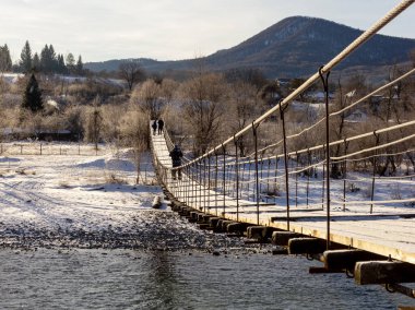 Kış günü, dağ nehri, donmayan bir dağ nehrinin üzerindeki çelik kabloların üzerinde asılı köprü, diğer tarafa gitmek için bir yol..