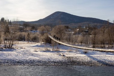 Kış günü, dağ nehri, donmayan bir dağ nehrinin üzerindeki çelik kabloların üzerinde asılı köprü, diğer tarafa gitmek için bir yol..