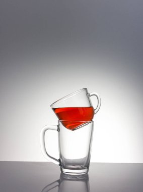 Kırmızı bir sıvıyla dolu temiz bir cam bardak, başka bir boş fincana monte edilmiş bir masa üzerinde bir mat bitiş gün ışığı ışınları, yakın plan, renkli bir arka plan.