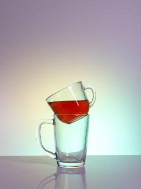 Kırmızı bir sıvıyla dolu temiz bir cam bardak, başka bir boş fincana monte edilmiş bir masa üzerinde bir mat bitiş gün ışığı ışınları, yakın plan, renkli bir arka plan.