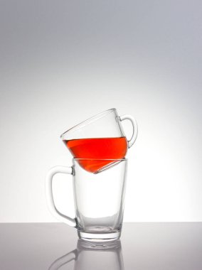 Kırmızı bir sıvıyla dolu temiz bir cam bardak, başka bir boş fincana monte edilmiş bir masa üzerinde bir mat bitiş gün ışığı ışınları, yakın plan, renkli bir arka plan.