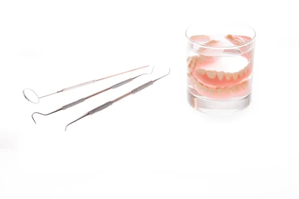 Dentures in glass of water and tools on white background — Stock Photo, Image