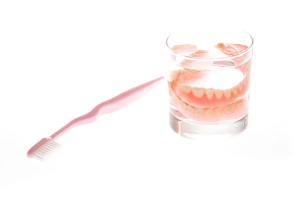 Dentures in glass of water and toothbrush — Stock Photo, Image