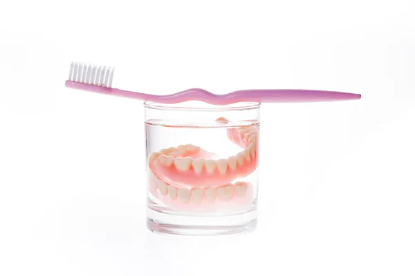 Dentures in glass of water and toothbrush — Stock Photo, Image