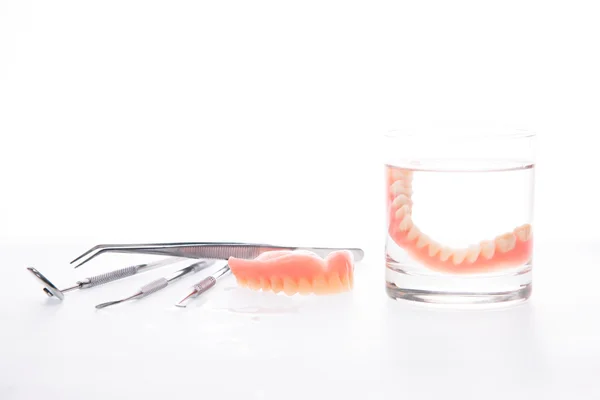 Prótesis dentales completas y herramientas con agua sobre fondo blanco — Foto de Stock