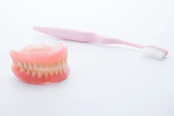 Dentiere acriliche con spazzolino da denti su sfondo bianco — Foto Stock