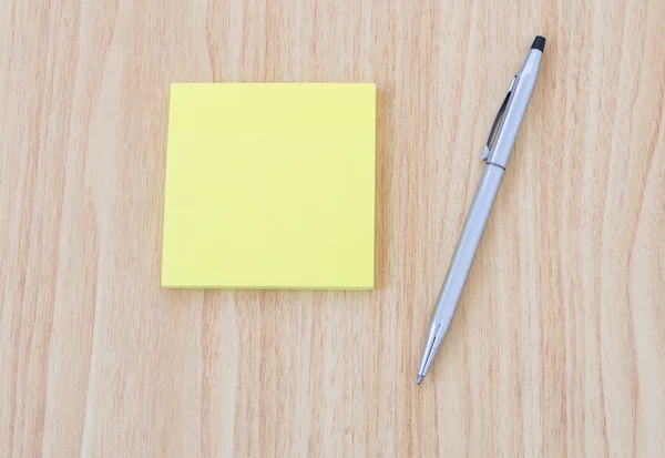 Bloc de notas amarillo en blanco con pluma en la mesa de madera de la oficina —  Fotos de Stock