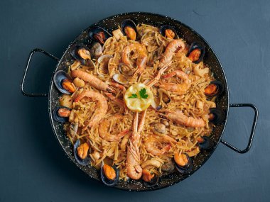 Fideua, noodle paella with seafood on rustic background, top view clipart