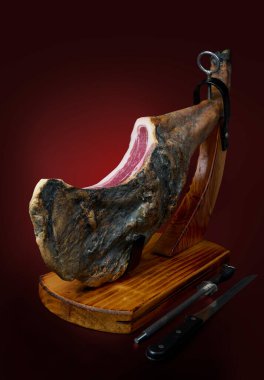 İspanyol İber jambonu ahşap destekte. Kırmızı koyu arkaplanda izole