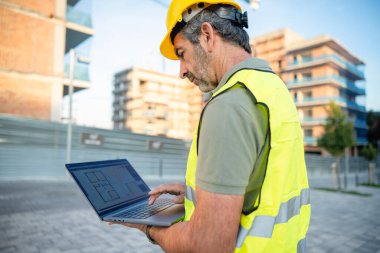 Engineer working on laptop with blueprint software at a construction site