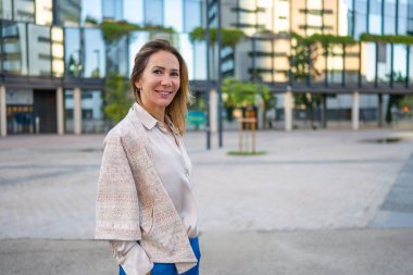 Middle aged woman smiling, standing outdoors in front of a modern building