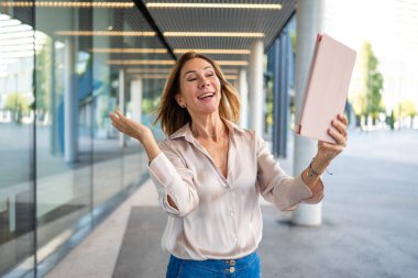 Businesswoman video calling on tablet while walking outside modern office building