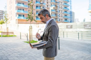 Experienced architect reviewing construction plans on a laptop outdoors