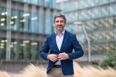 Businessman buttoning his jacket while standing confidently in front of a modern office building